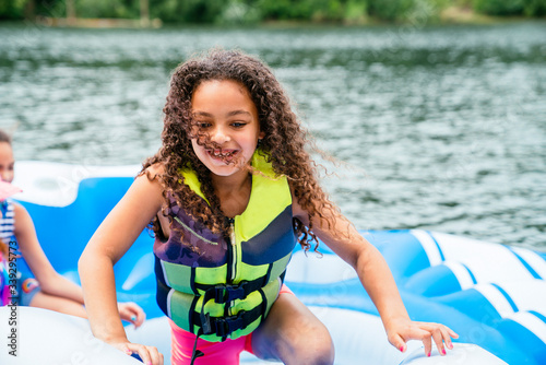 Obraz na plátně Smiling happy girl in life jacket with long curly hair playing on floaty on lake