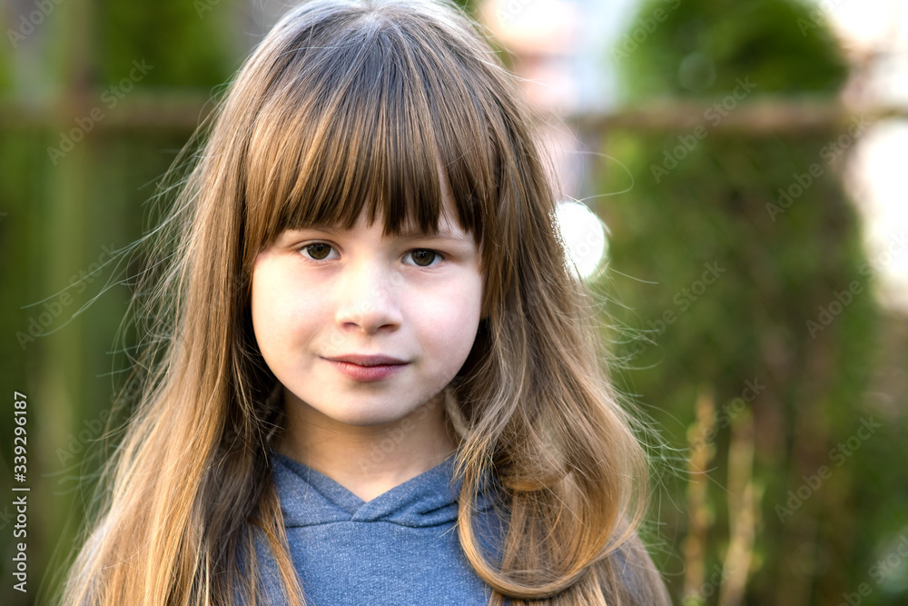 Portrait of pretty child girl with gray eyes and long fair hair smiling outdoors on blurred green bright background. Cute female kid on warm summer day outside. Portrait of pretty child girl with gray eyes and long fair hair smiling outdoors on blurred green bright background. Cute female kid on warm summer day outside.