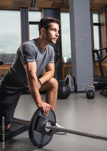 Fit young man working out with heavy weights standing on one knee pulling the barbell up