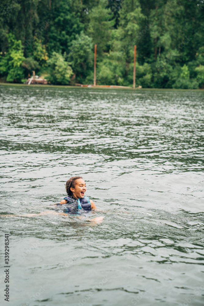 Happy smiling girl swimming in lake with life preserver on