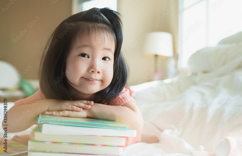 Image of Asian Toddler portrait shot while her proud and talking to present her book stack, Concept little bookworms enjoy learning to be intelligent kids, Adorable child reading book for preschool. Image of Asian Toddler portrait shot while her proud and talking to present her book stack, Concept little bookworms enjoy learning to be intelligent kids, Adorable child reading book for preschool.