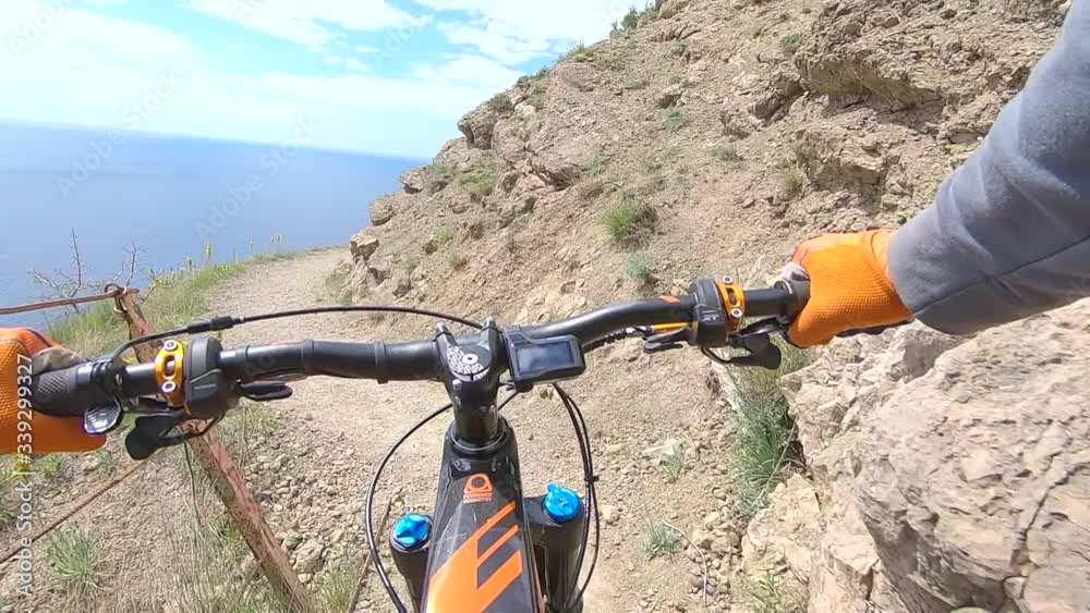 Point chest view from action camera bicycle handlebar and hands while riding on cliff edge trail along sea. Bicyclist holding handle wheel while riding on rocky mountain route on enduro mtb bike