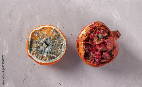 Spoiled rotten foods with mold: half an orange and pomegranate on gray background, Top view