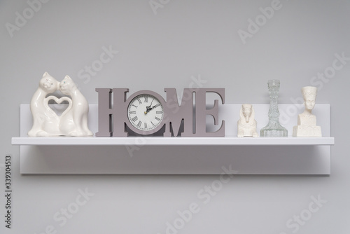 White shelf on a gray wall with a clock decorative Egyptian figurines and decorative cats. Beautiful shelf. Design for home.