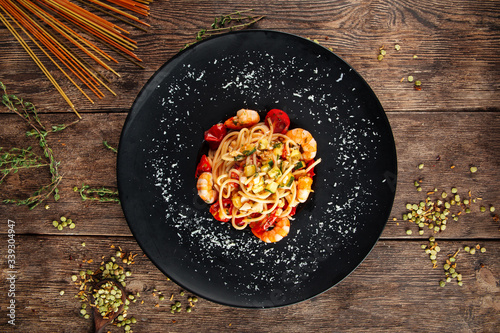 Top view on spaghetti with shrimps and parmesan cheese in a black plate on the wooden table, horizontal format