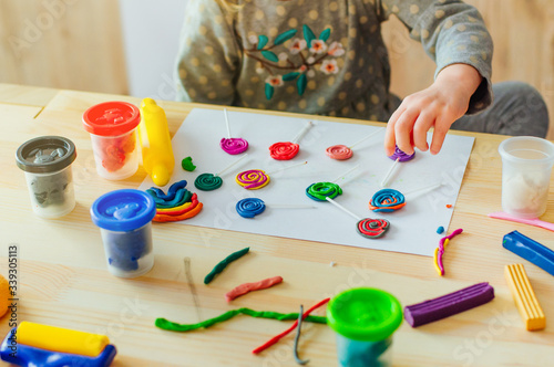 Little girl molding colorful clay lollipops on the wooden table