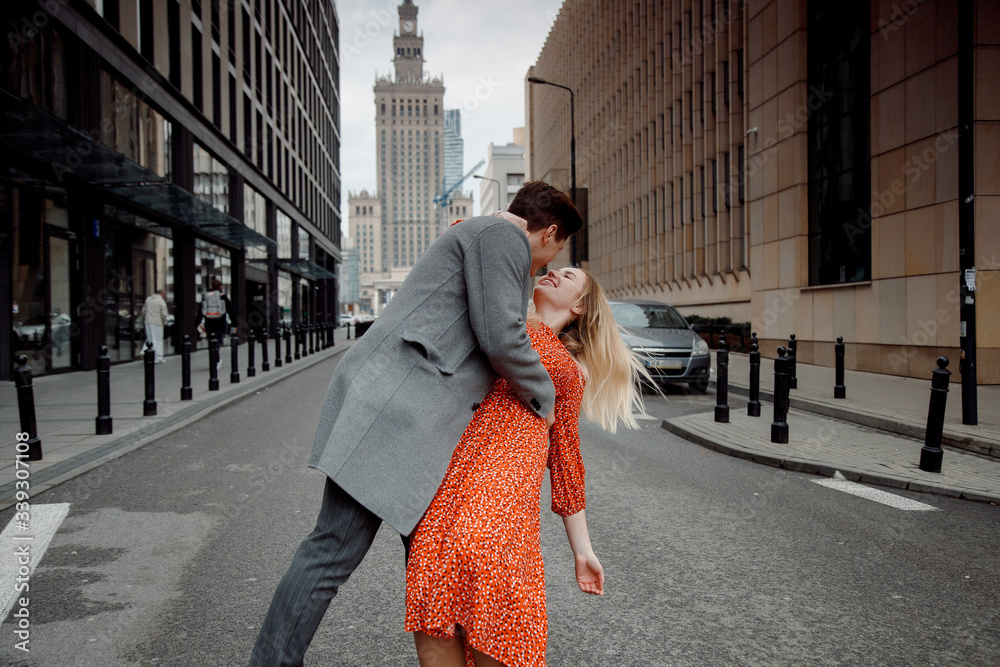 Fototapeta premium tourist couple in big city. The guy with the girl is hugging and happy. Girl in red dress kissing boy.