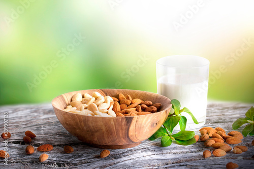 Spring almonds or nuts in brown bowl with glass of milk on wooden vintage table. Green garden blurred background.