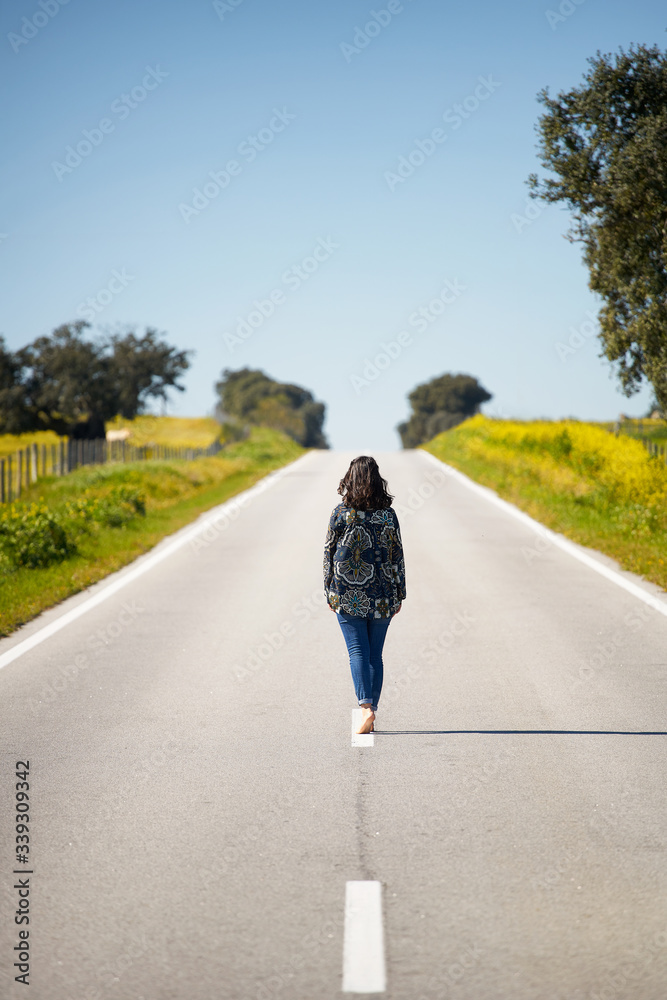 Woman walking on the middle of a road in beautiful yellow flowers landscape in Alentejo, Portugal