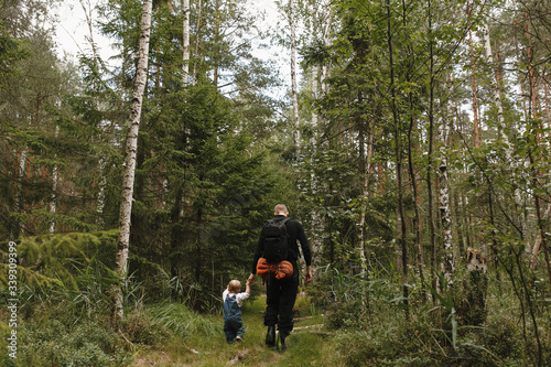 Back view of father and one-year-old daughter walking hand in hand in forest