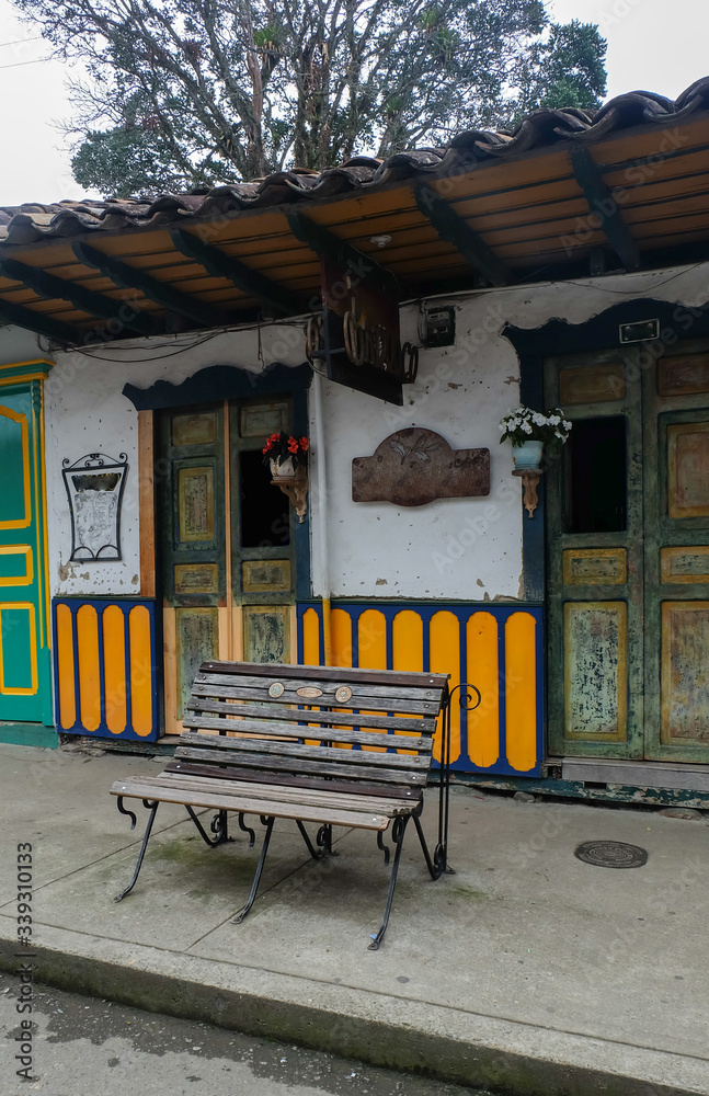 Public wood and iron chair in front of colorful rustic house