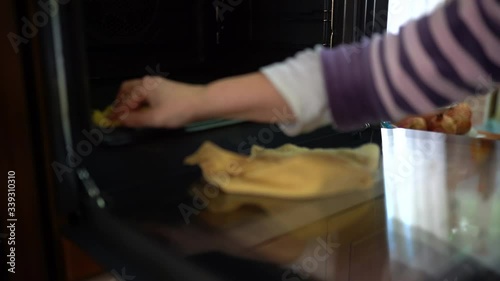 Close-up of housewife's hands using wet yellow rag and sponge with chemicals for cleaning inside stove, removing dirty and greasy surface and other different spots. Cleaning oven with degreaser and photo