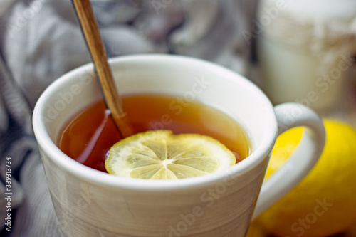 Hot black tea with a slice of lemon in a large gray mug with a spoon closeup, top view, next to dried oranges, fresh lemon, brown sugar, gray napkin on a wooden tray. The concept of a cozy home tea 