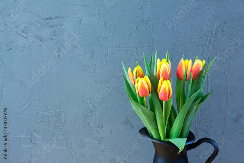Red and yellow tulips in black jug with grey backround. Spring tulips.