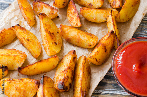 Golden spicy potato wedges fried or oven baked with ketchup on wooden table.