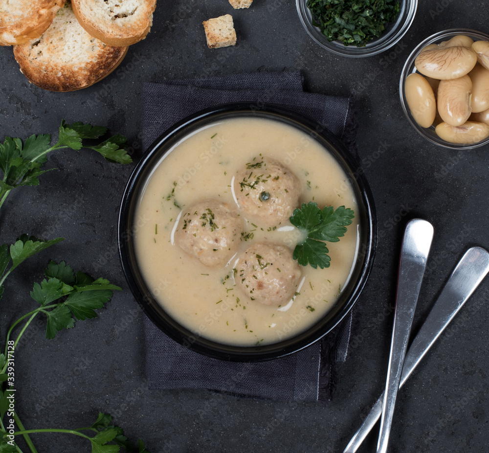 Bean soup-puree with meatballs, dill, parsley and croutons in a bowl on a dark background top view