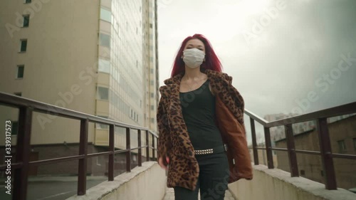 Concept: urban healthcare during pollution pandemic. Beautiful young asian girl with colored hair in medical mask wearing grunge fashion clothing walk street