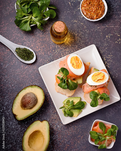 Healthy toasts with smoked salmon and avocado served with mustard, eggs and leafy greens on black table top. Mediterranean diet snack, open sandwich