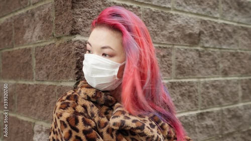 Concept: urban healthcare during pollution pandemic. Beautiful young asian girl with colored hair in medical mask wearing grunge fashion clothing standing street
