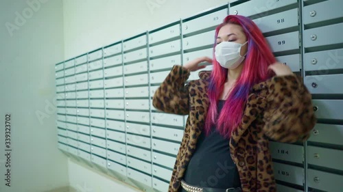 Concept: urban healthcare during pollution pandemic. Beautiful young asian girl colored hair medical mask grunge fashion clothing standing near mailboxes in apartment house