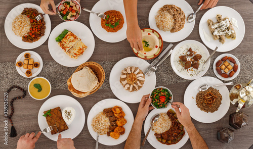 Iftar. Arabic family dinner after fasting. People sharing plates by hands. Ramadan Kareem, Eid Mubarak. Top view of table with food. Lebanese cuisine. Muslim people.