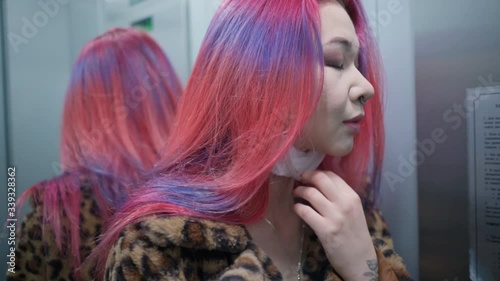Concept: urban healthcare during pollution pandemic. Beautiful young asian girl colored hair check medical mask in mirror grunge fashion clothing ride elevator apartment house