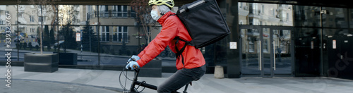 Courier wearing medical mask and gloves riding a bicycle to deliver food order to customers during virus outbreak. Coronavirus, COVID-19, safe delivery