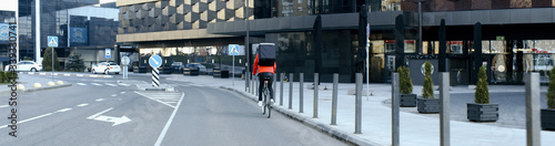 Courier wearing medical mask and gloves riding a bicycle to deliver food order to customers during virus outbreak. Coronavirus, COVID-19, safe delivery