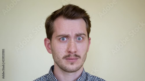 A handsome young man, with stubble and moustache and beautiful hairstyle, is surprised at the lack of understanding and is afraid. Studio portrait cover is white. he has beautiful teeth and blue eyes.