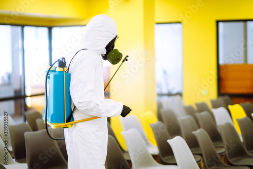 Man wearing protective suit disinfecting assembly hall with spray chemicals to preventing the spread of coronavirus, pandemic in quarantine city. Disinfecting of office. COVID-19. © maxbelchenko