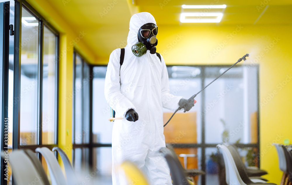 Man wearing protective suit disinfecting assembly hall with spray chemicals to preventing the spread of coronavirus, pandemic in quarantine city. Disinfecting of office. COVID-19. Man wearing protective suit disinfecting assembly hall with spray chemicals to preventing the spread of coronavirus, pandemic in quarantine city. Disinfecting of office. COVID-19.