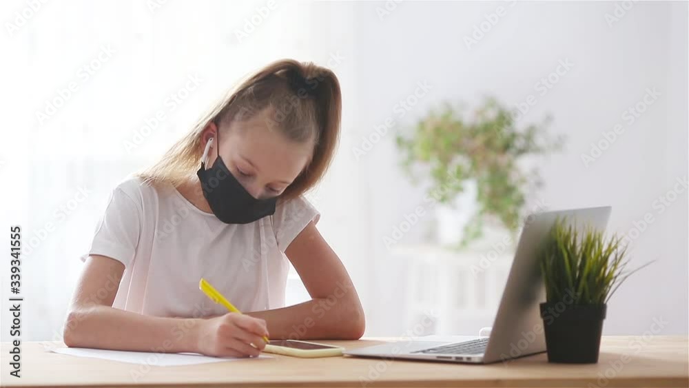 Serious schoolgirl sitting at table with laptop and textbook and doing homework. Serious schoolgirl sitting at table with laptop and textbook and doing homework.