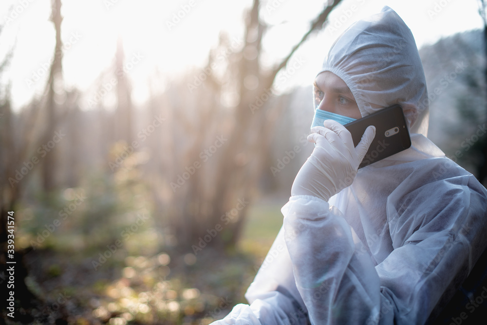 man in protective clothes sitting in a forest and talking on the phone, in background trees and branches man in protective clothes sitting in a forest and talking on the phone, in background trees and branches