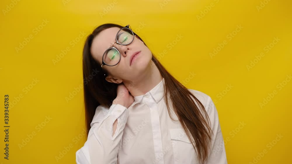 Tired woman in eyeglasses feeling stiff sore neck pain concept rubbing massaging tensed muscles suffer from fibromyalgia, has gloomy expression, isolated on yellow background. Fibromyalgia concept Tired woman in eyeglasses feeling stiff sore neck pain concept rubbing massaging tensed muscles suffer from fibromyalgia, has gloomy expression, isolated on yellow background. Fibromyalgia concept