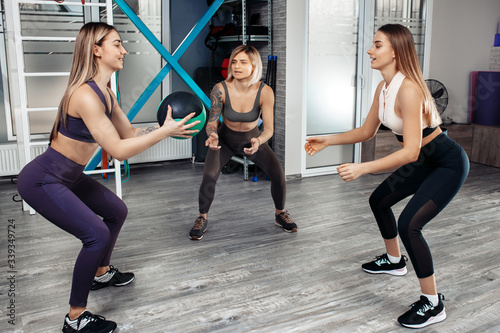 Group of three young sporty girls workout with medicine ball in fitness class.