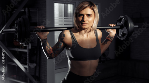 Young sporty blonde woman doing heavy barbell exercise in fitness class.
