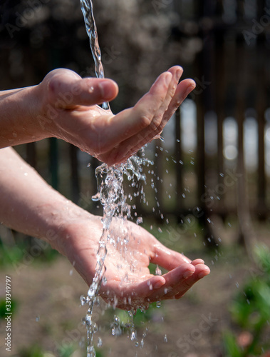 Strong male hands under a stream of water on a blurred natural background.