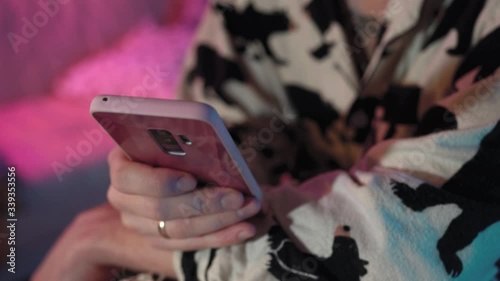 a man is typing on his phone and sitting in a room with colored lights.the man is dressed in pajamas