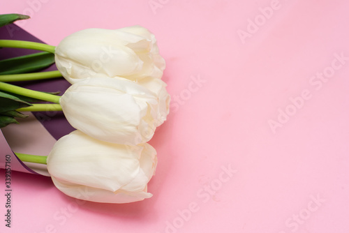 Bouquet of white tulips wrappen in pink paper. Minimal nature flat lay. Greeting card for Mother's Day and March 8th. Tender concept of spring holidays