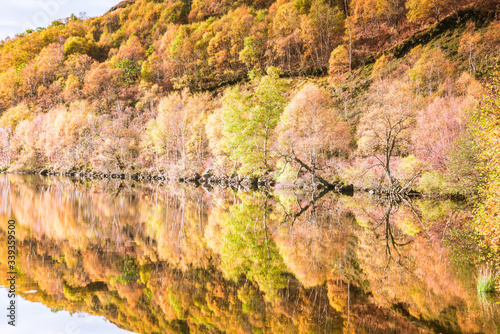 Autumn colours in Highlands of Scotland - trees, mountains, sky, hills, stones reflected in loch waters photo