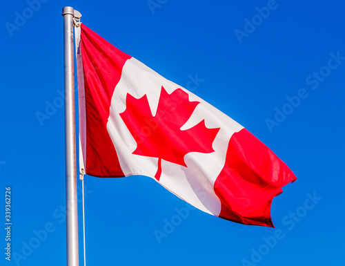 A Canadian flag flying in the blue sky.