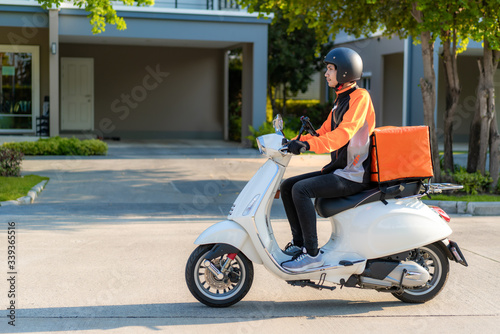 Asian man courier on scooter delivering food in town streets with a hot food delivery from take aways and restaurants to home photo