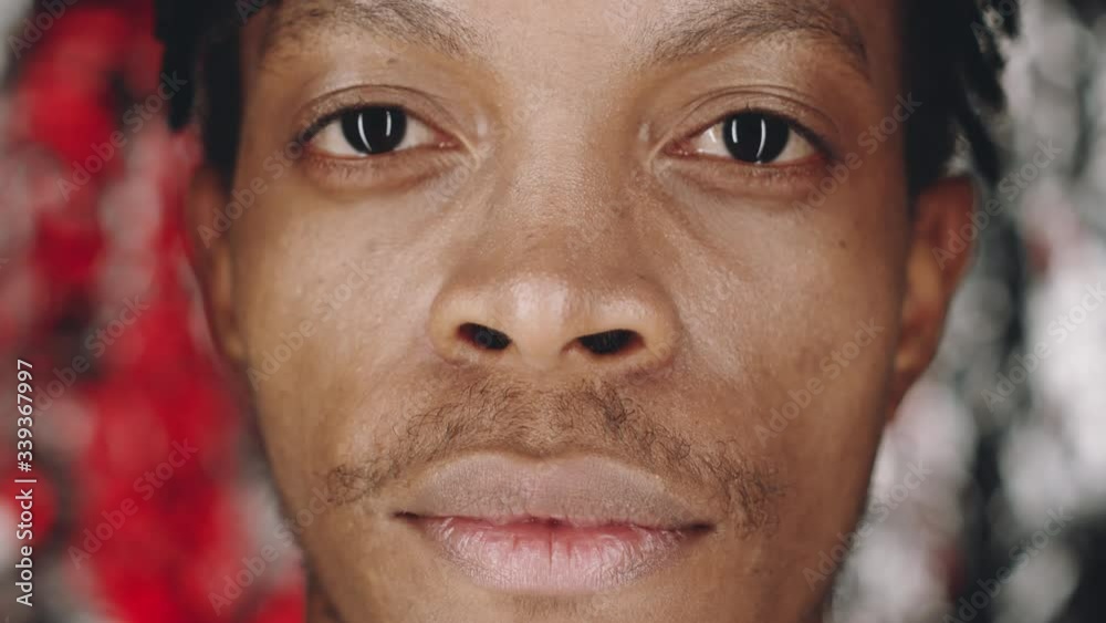 Macro shot of face of young handsome African American man raising his head, looking at camera and smiling while posing in studio Macro shot of face of young handsome African American man raising his head, looking at camera and smiling while posing in studio
