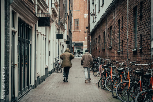 Two men go on empty Amsterdam downtown street with closed bars, restaurants and stores due to outbreak of Coronavirus Covid-19 infection, quarantine time.