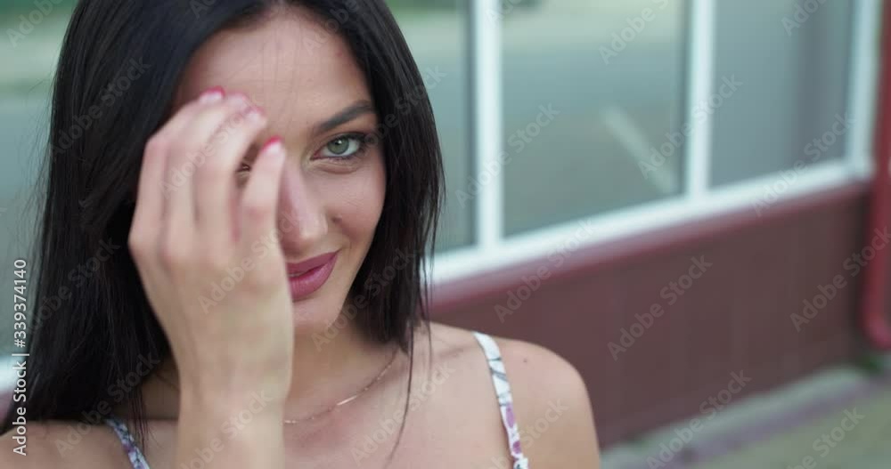 Enigmatic brunette corrects her hair and smiles at camera on street Enigmatic brunette corrects her hair and smiles at camera on street