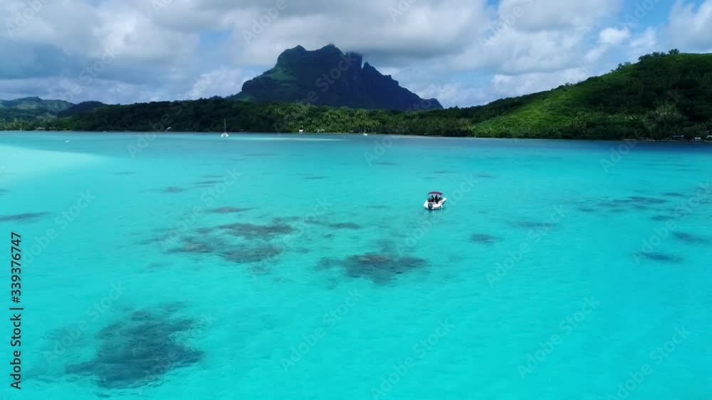 Beautiful drone shot of a speedboat in tropical island honeymoon destination island Bora Bora, French Polynesia. Boat floats in the blue turquoise water mountain peaks dot the coastline landscape Beautiful drone shot of a speedboat in tropical island honeymoon destination island Bora Bora, French Polynesia. Boat floats in the blue turquoise water mountain peaks dot the coastline landscape