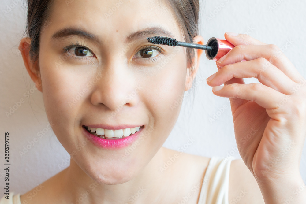 Close-up of young Asian woman applying black mascara on her eyelashes with makeup brush. Mascara is a cosmetic commonly used to enhance the eyelashes.