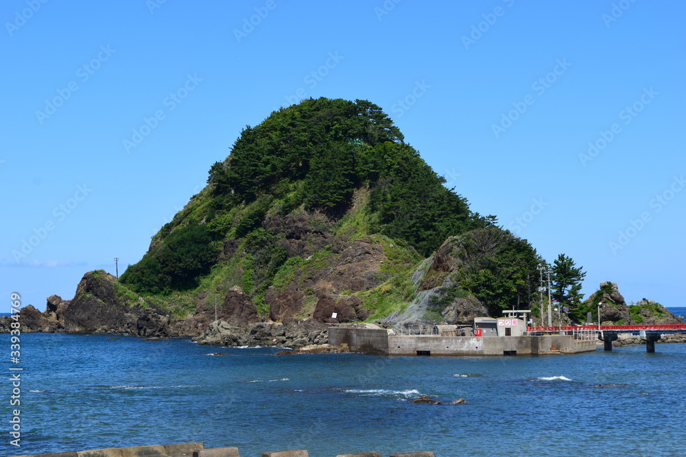 Obraz premium 白山島(東北の江ノ島)/ 山形県鶴岡市の由良海岸沖にある白山島は、「日本の渚百選」と、「快水浴場百選」に選ばれた由良海岸のシンボル的な島で、その景観から「東北の江ノ島」と呼ばれています。由良海岸から島までは赤い白山橋が架けられており、歩いて島に渡ることが出来ます。