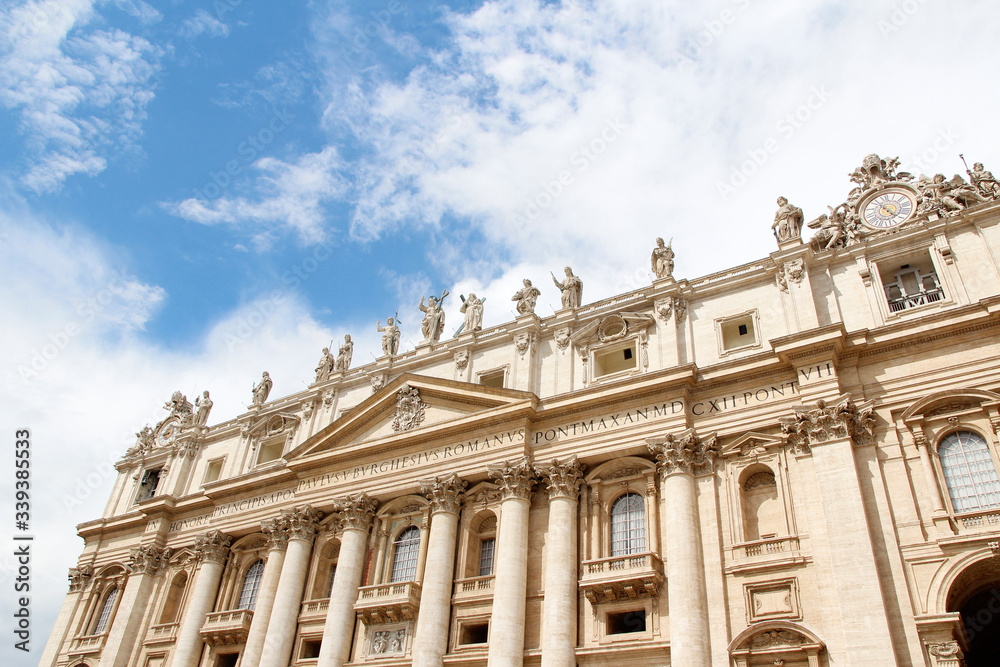 Statues of Christ and the Apostles and Oltramontano Clock on top of the facade of St Peter's Basilica with blue sky and clouds in Vatican City
