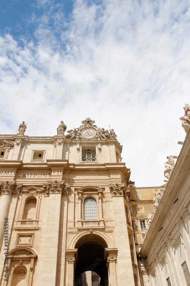 Fototapeta premium Statues of Christ and the Apostles and Oltramontano Clock on top of the facade of St Peter's Basilica with blue sky and clouds in Vatican City